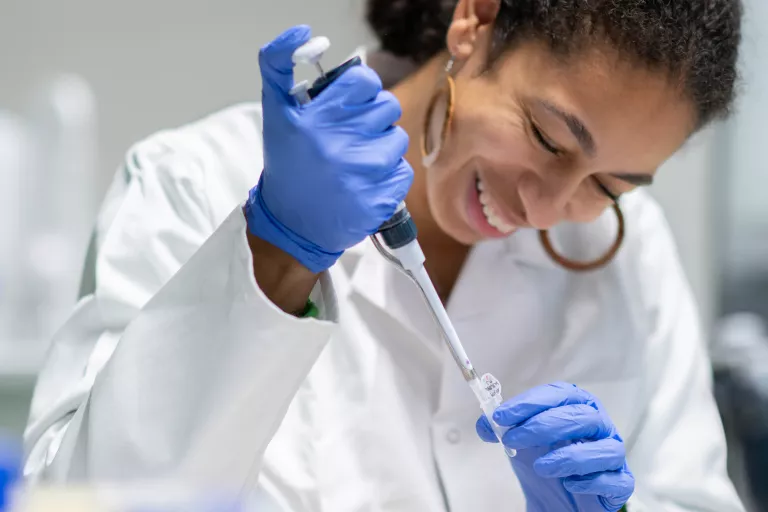 PhD student Dufie smiling and pipetting in the lab