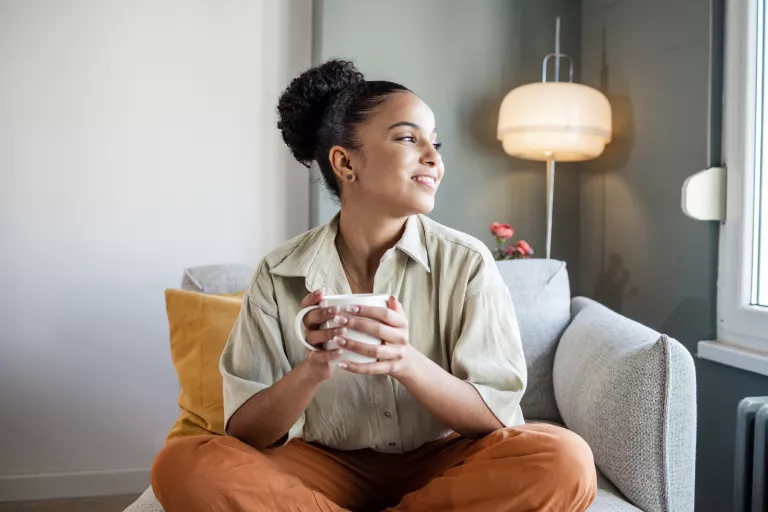 Stock image of a person sitting cross-legged in an armchair drinking a warm beverage and smiling
