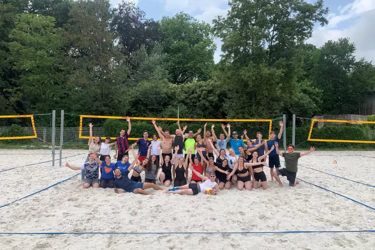 PhD students posing and smiling on a beach volleyball court