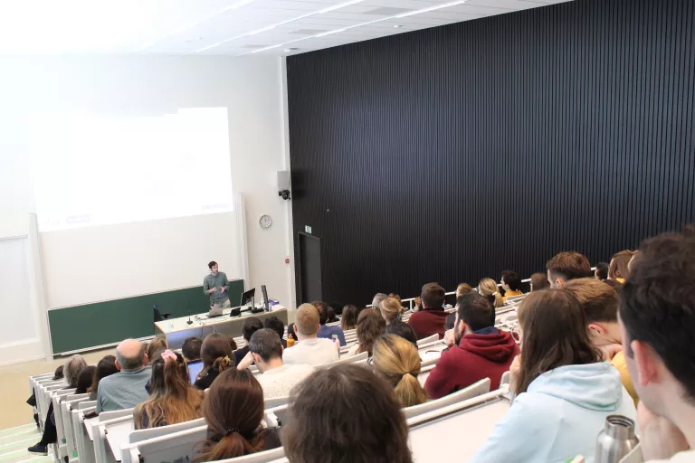 A PhD student giving a progress seminar to a room full of researchers in the auditorium at the VIB-KU Leuven Center for Brain &amp; Disease Research