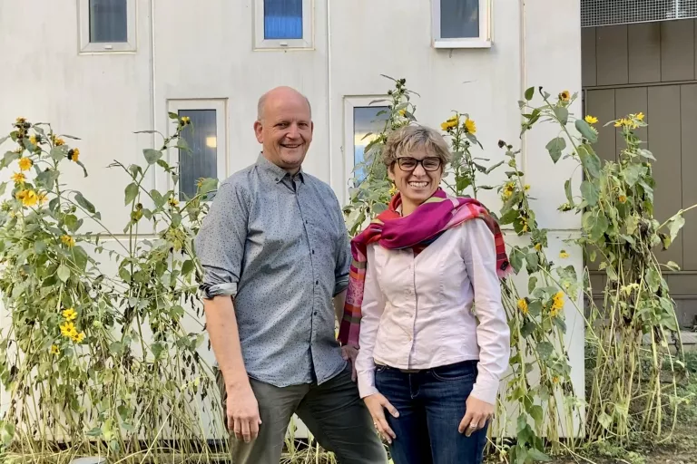 Eco Team leads standing and smiling in front of tall plants outside the Center