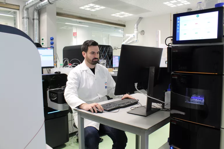 Proteomics expert Pedro Magalhães in a lab coat in a room full of computers and mass spectrometry equipment at the VIB Metabolomics Core