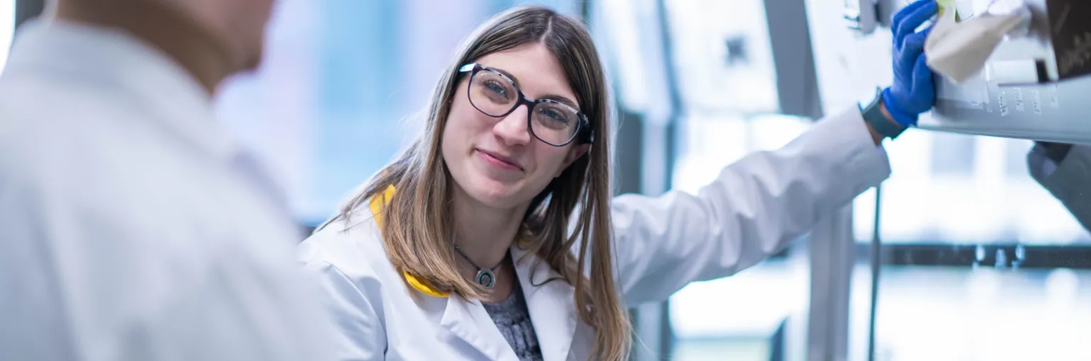 A scientist smiling, leaning against a cell hood and chatting with a colleague at the VIB-KU Leuven Center for Brain &amp; Disease Research